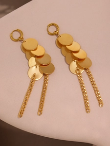 Détail de boucles d'oreilles pendantes dorées mates avec disques superposés et pompons