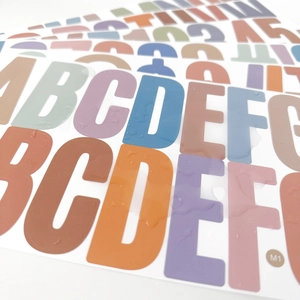 Macro shot of 2.5-inch Morandi letter stickers showing waterproof coating with water drops