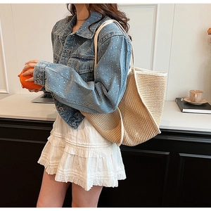Detail of a beige woven tote bag paired with denim jacket and white tiered skirt