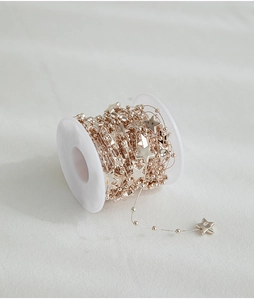 Detail of rose gold star bead chain on white spool for Christmas tree decoration