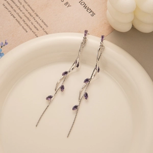 Macro detail of long leaf tassel earrings with purple gemstones on a ceramic dish