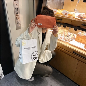 Détail d'une grande trousse à maquillage en toile à carreaux orange tenue par un modèle