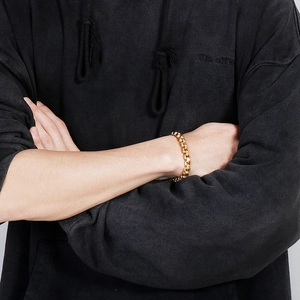 Close-up of a polished gold men's chunky link chain bracelet worn on a hoodie sleeve