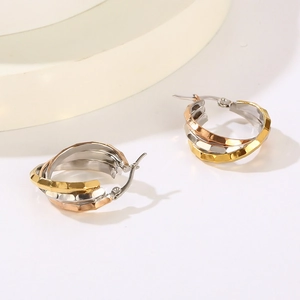 Detail of interlocking tricolor hoop earrings in gold silver and rose gold with faceted texture