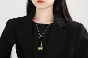 Close-up of golden double heart tassel necklace on model wearing a black blazer