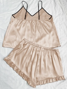 Detailed view of champagne silk pajama set featuring black trim and ruffle hem shorts
