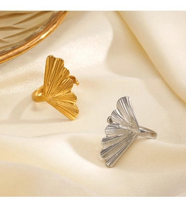 Detailed view of gold and silver ginkgo leaf rings on a soft beige silk fabric