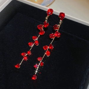 Macro shot of long red tassel earrings with gold chains on black velvet jewelry box
