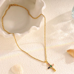 Detailed shot of a gold cross necklace with multicolored gemstones on a seashell tray
