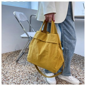 Detailed view of yellow nylon tote bag worn by a model in a bright indoor setting