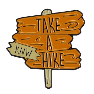 Macro view of hiking signpost enamel pin with Take A Hike text and orange finish