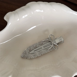 Macro view of a silver sword-shaped metal hair clip with a bow and rhinestones in a shell dish