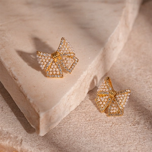 Close-up of golden bow earrings featuring micro-pave cubic zirconia and pearl details