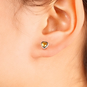 Close-up of yellow heart-shaped stud earring with silver setting worn on earlobe