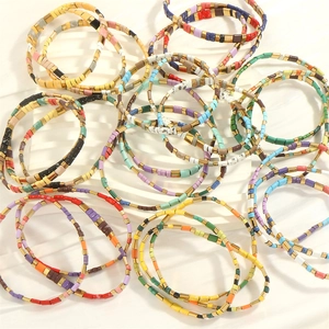 Macro shot of bohemian TILA beaded stretch bracelets with colorful enamel tiles on white stand