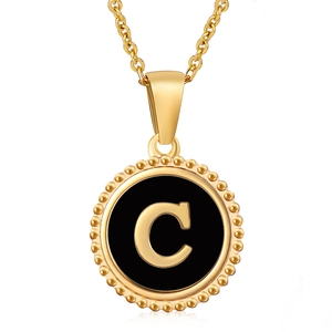Detail of a round gold necklace pendant featuring a black inlay and golden letter C