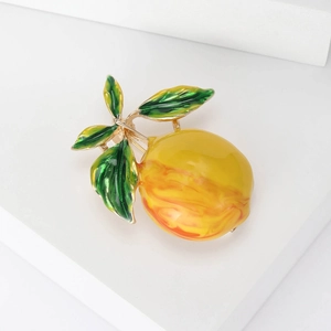 Enamel lemon brooch with yellow-orange gradient and green leaves on a white stand