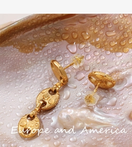 Macro detail of golden U-shaped link earrings with glossy finish on shell background