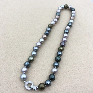 Detailed shot of multi-color pearls in peacock green and gold with a diamond fish clasp