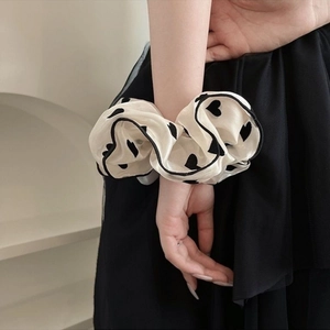 Chic cream scrunchie with black heart print worn on wrist for a stylish hair accessory look