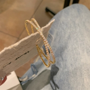 Dettaglio di orecchini a cerchio intrecciati dorati con micro-pave di zirconi