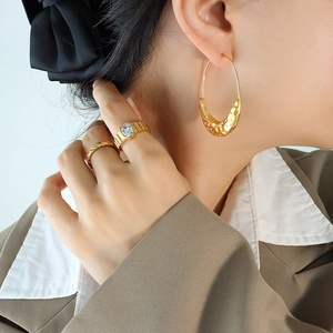 Textured boat-shaped hoop earrings and gold rings with 18K plating on a model