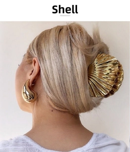 Detailed close-up of a golden shell hair claw and teardrop earring on a model