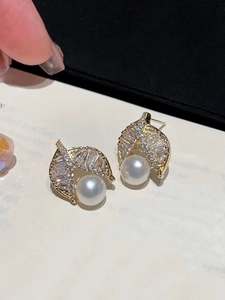 Detailed close-up of gold leaf stud earrings with clear zircon stones and white pearls