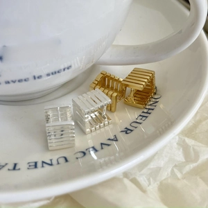 Detail view of gold and silver hollow square earrings on a white ceramic plate