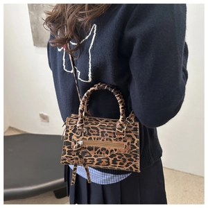 Dettaglio della borsa leopardata con nappa e manici intrecciati su una modella