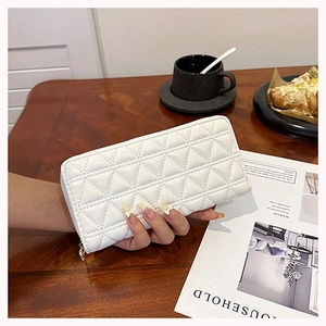 Detailed view of white quilted long wallet with golden zipper held in a cozy cafe setting