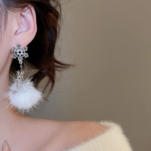 Detail view of snowflake reindeer earrings with white fur balls worn by a model