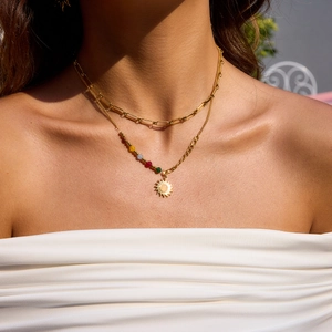 Detail of layered gold stainless steel necklace with sun pendant and colored beads