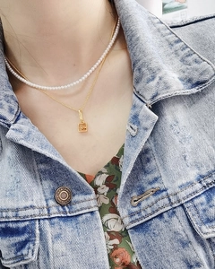 Detail of a double-layered gold necklace with pearls and a square hollow pendant