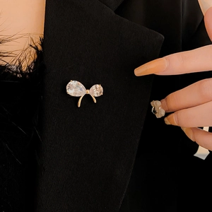 Close-up of a gold-plated bow brooch with clear cubic zirconia on black blazer fabric