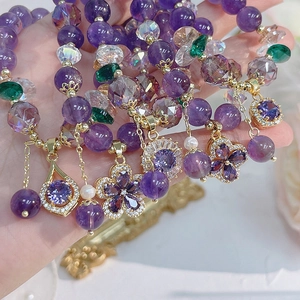 Close-up of hand holding purple amethyst bracelet with zircon flower and pearls