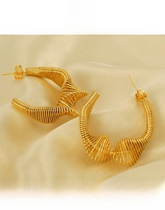 Detail of gold-plated titanium steel spiral hoop earring on champagne silk background