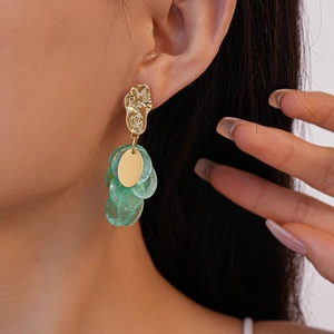 Close-up of geometric gold earrings with green circular pendants on female model