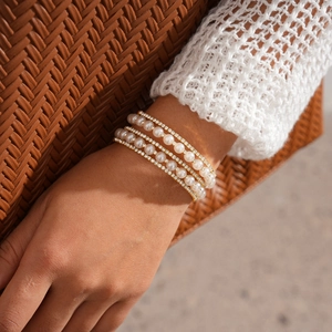 Detailed view of layered pearl and gold diamond bracelet on model with knit sleeve
