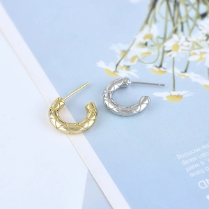 Macro detail of gold and silver C-shaped earrings with elegant quilted texture finish