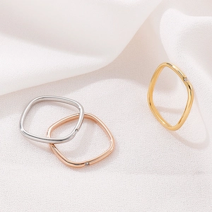 Detailed view of silver, rose gold, and gold square rings with diamonds on white fabric
