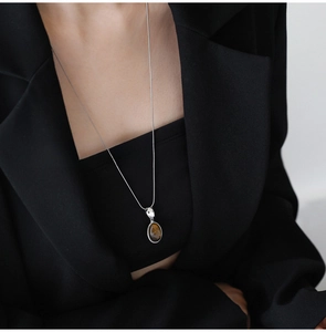 Macro detail of oval tiger eye stone pendant on sleek silver snake chain necklace