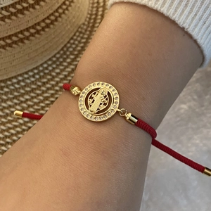 Macro detail of red woven bracelet with micro-pave gold religious medallion on model