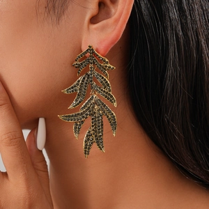 Détail de boucles d'oreilles feuille vintage dorées avec strass noirs portées par le mannequin