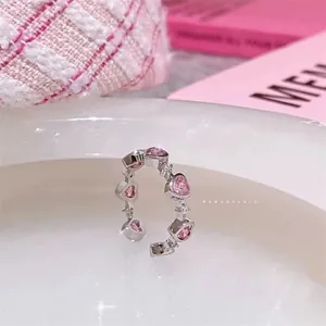 Close-up of pink heart-shaped gems and white diamonds on an open silver ring band
