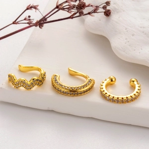 Close-up of three gold-plated clip earrings with sparkling cubic zirconia on a marble base