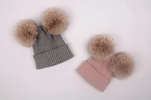 Détail de bonnets en tricot gris et rose avec doubles pompons en fausse fourrure brune