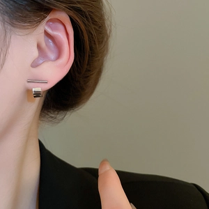 Macro close-up of minimalist silver geometric stud earrings worn on a model's ear lobe