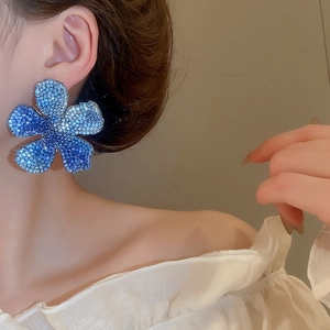 Close-up of model wearing large blue floral stud earrings with gradient crystal stones