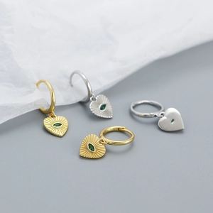 Detailed macro view of gold and silver heart-shaped earrings with green central gemstones